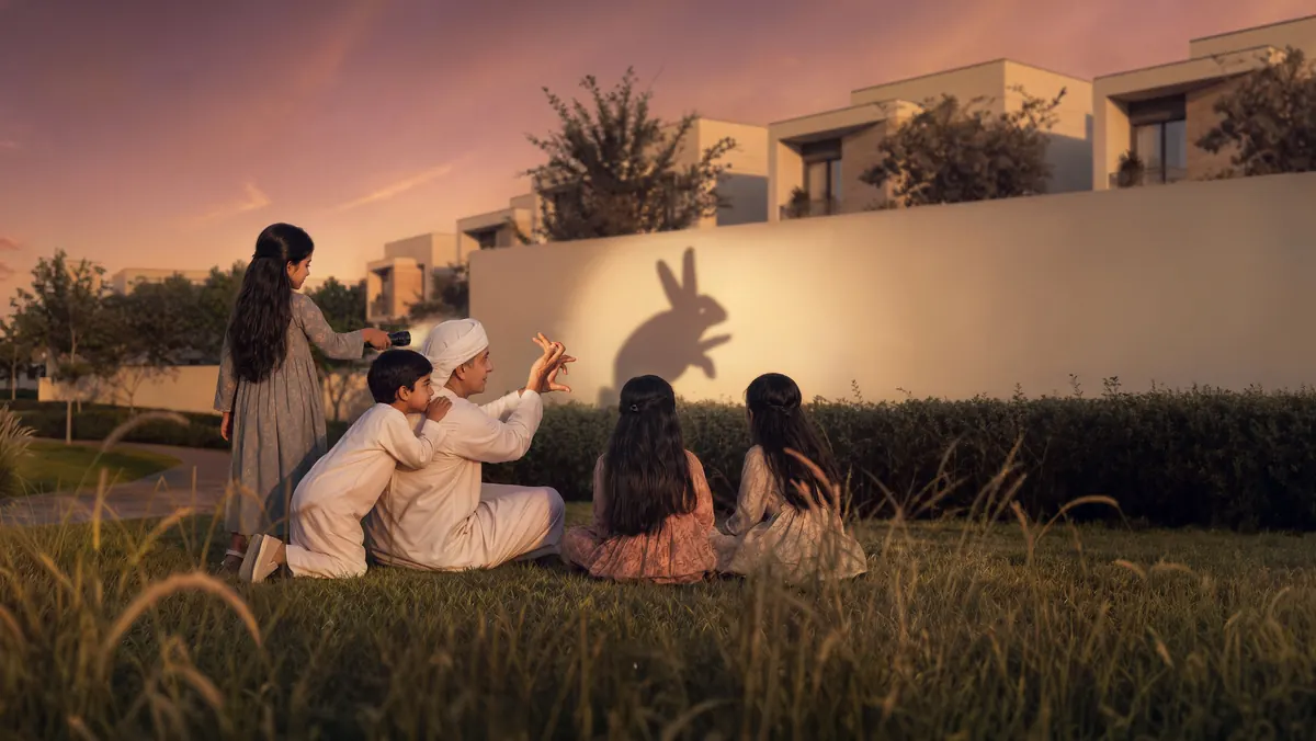 A family making shadow puppets on a garden wall at dusk